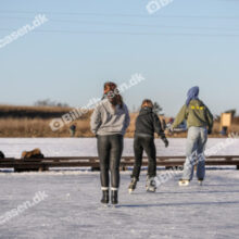 Skøjteløbere på frossen sø med gående i baggrunden
