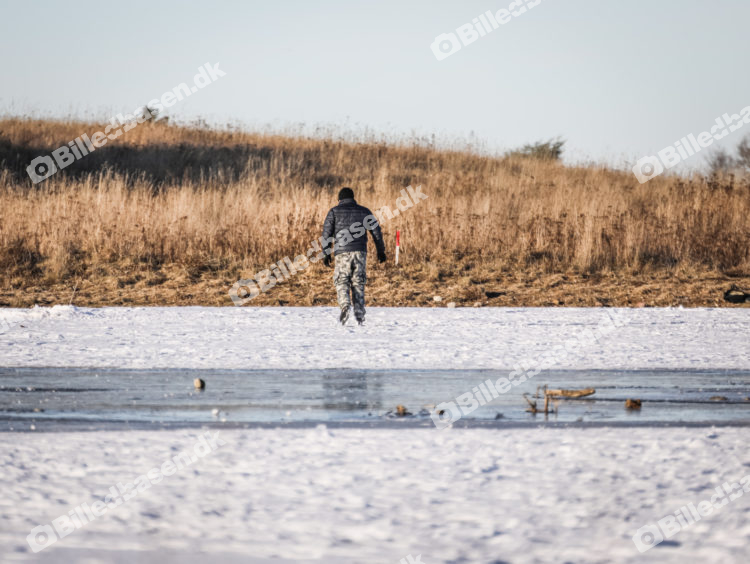 Skøjteløber på frossen sø med gående i baggrunden