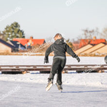 Skøjteløbere på frossen sø med gående i baggrunden